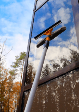 window cleaning with squeegee on tall glass building reflecting sky and trees